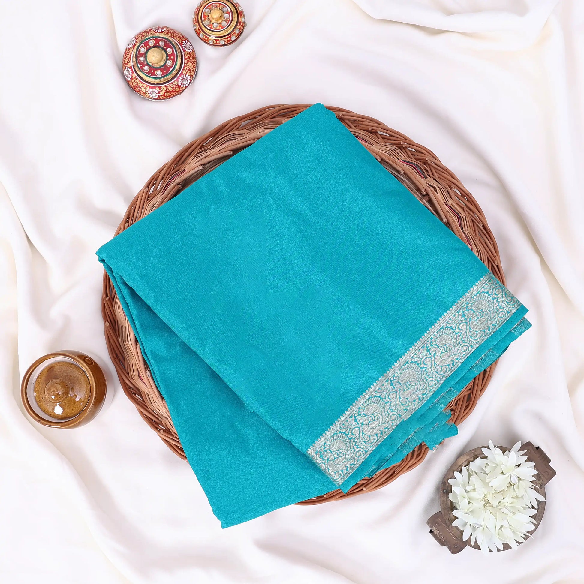 A folded turquoise blue saree  features a decorative light blue and white border pattern along one edge.