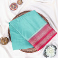 A folded turquoise and red patterned mysore silk saree with pink and golden border