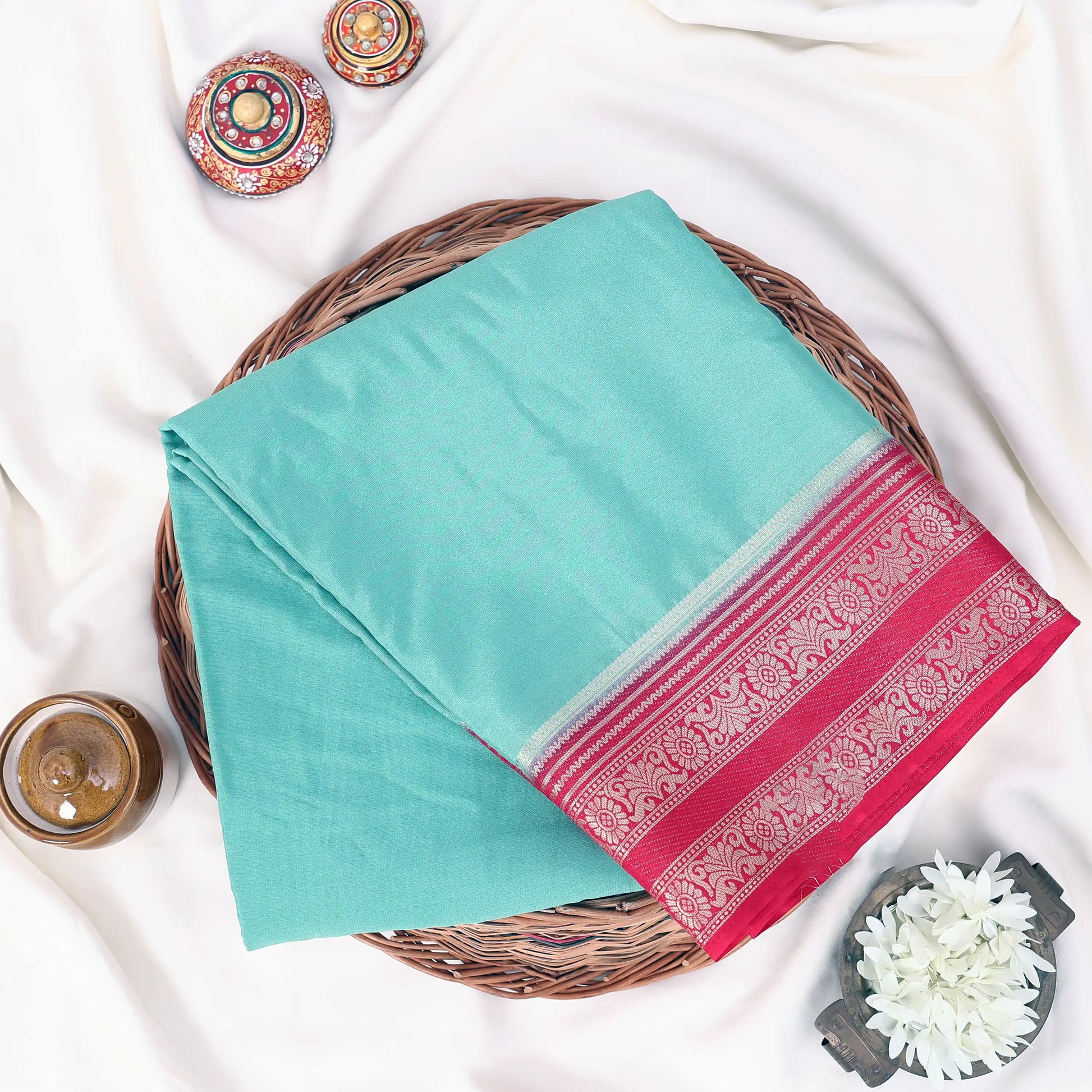 A folded turquoise and red patterned mysore silk saree with pink and golden border