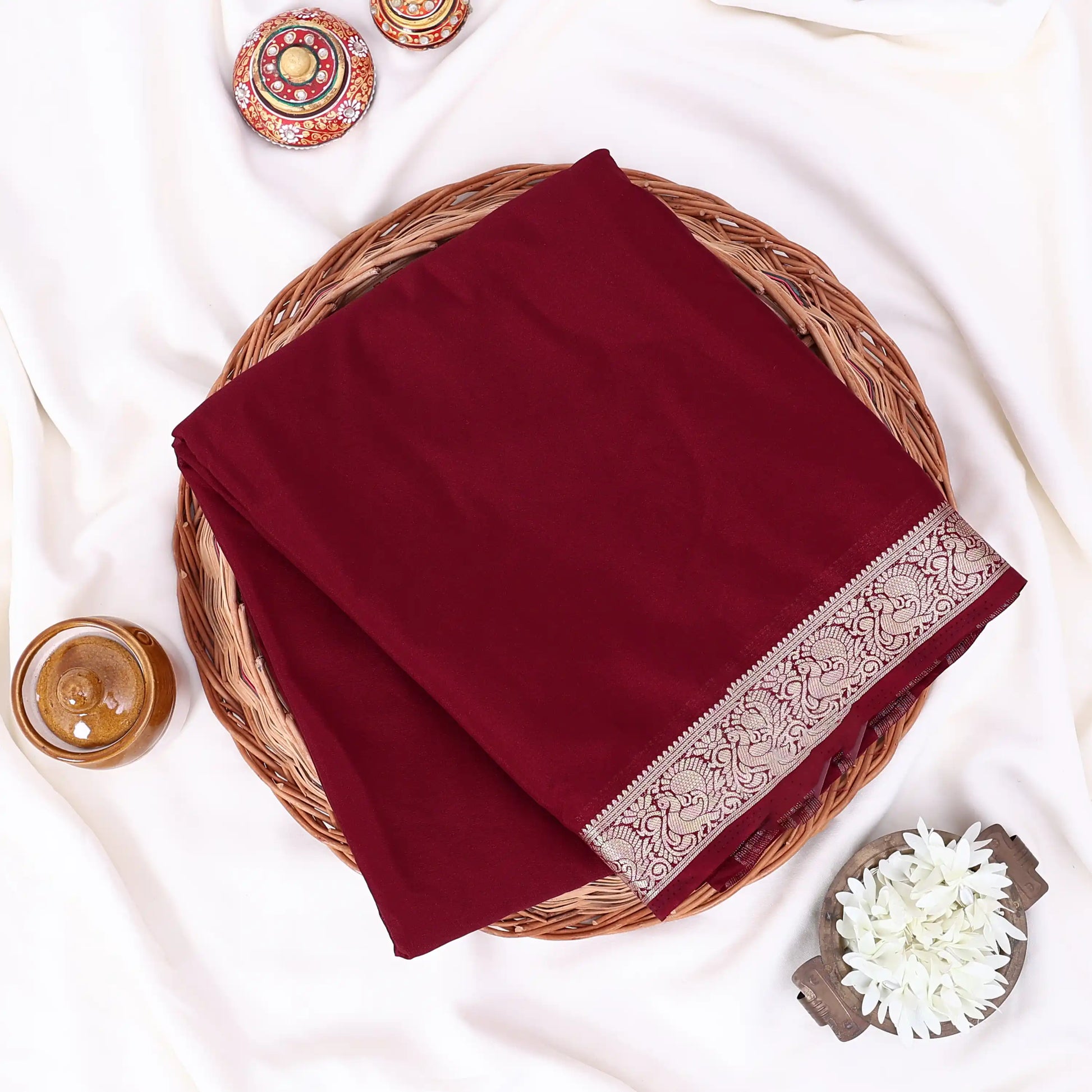 A folded deep maroon red saree,  featuring a detailed beige floral border