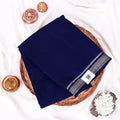 A folded navy blue saree features a decorative border with silver and white geometric patterns 