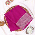A folded magenta pink saree features a decorative border with white and light pink geometric patterns.