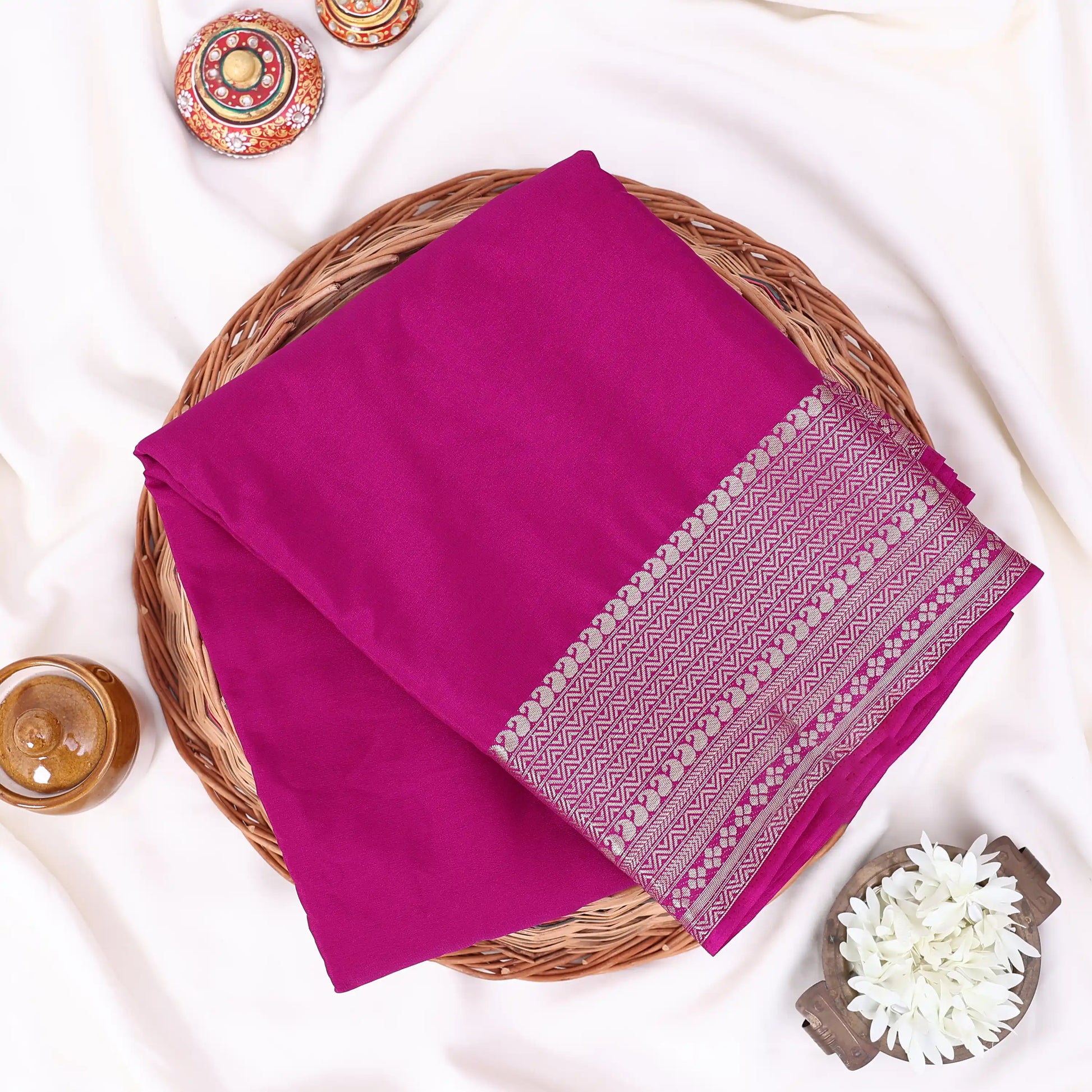 A folded magenta pink saree features a decorative border with white and light pink geometric patterns.