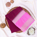 A folded purple mysore silk saree features a wide dark pink  border with a silver zari detailing.