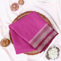 A folded magenta purple saree with a detailed silver and gold border