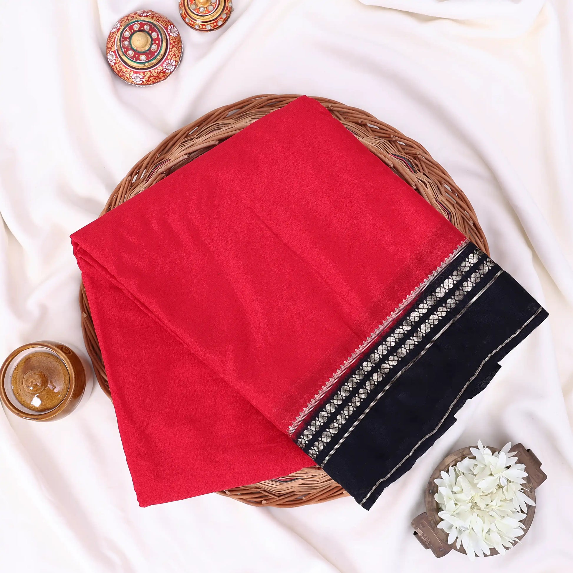 A folded redmysore silk saree features a prominent black border with intricate silver and white geometric patterns.