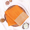 An orange saree features a decorative cream-colored embroidered border on one end.