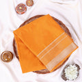 A folded orange mysore silk saree ifeatures a beige border with woven stripes.