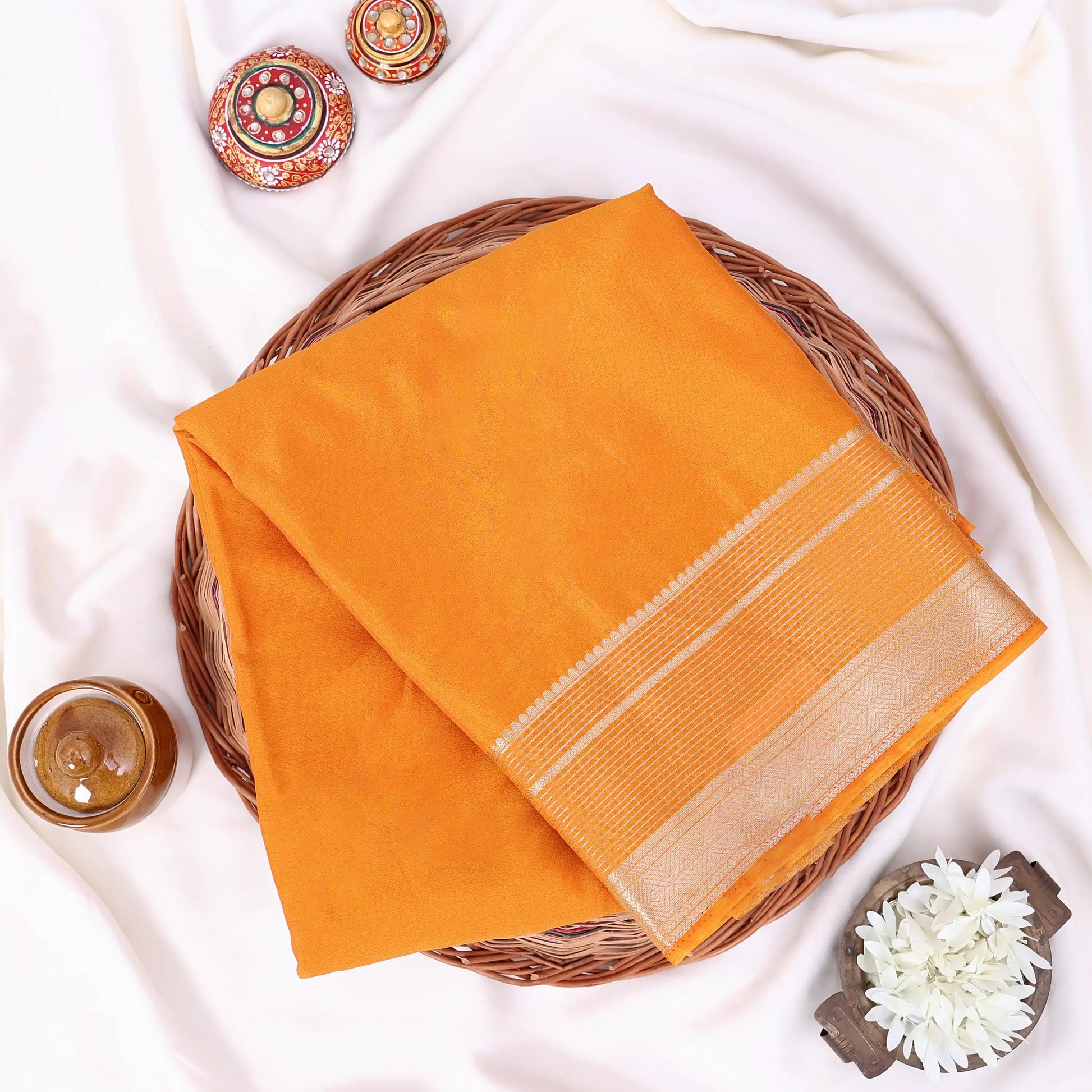 A folded orange mysore silk saree ifeatures a beige border with woven stripes.