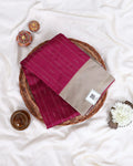 A folded deep magenta saree with thin vertical gold stripes and a beige border