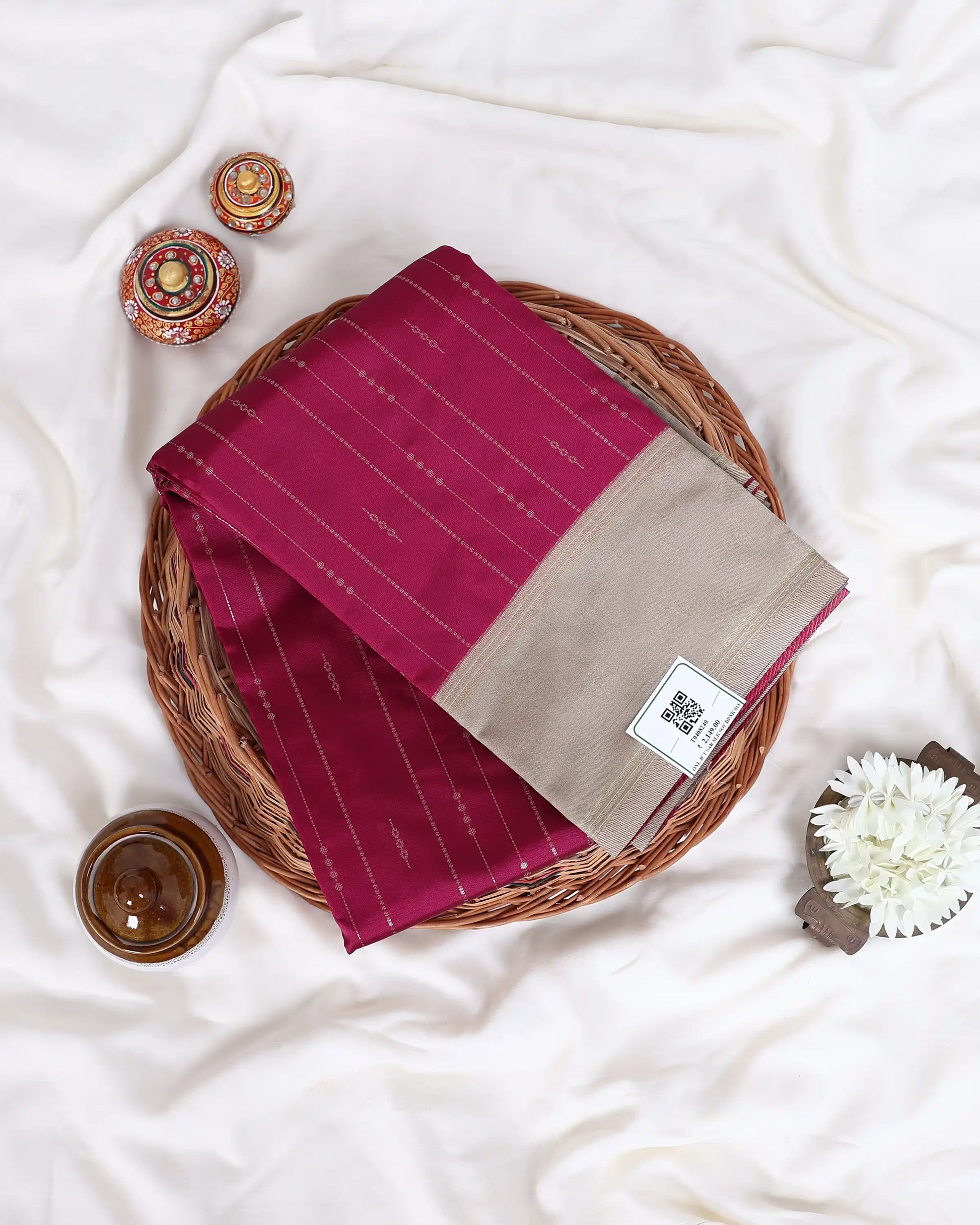 A folded deep magenta saree with thin vertical gold stripes and a beige border