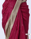 A close-up of a draped sari in deep magenta pink with thin white stripes and a wide beige border