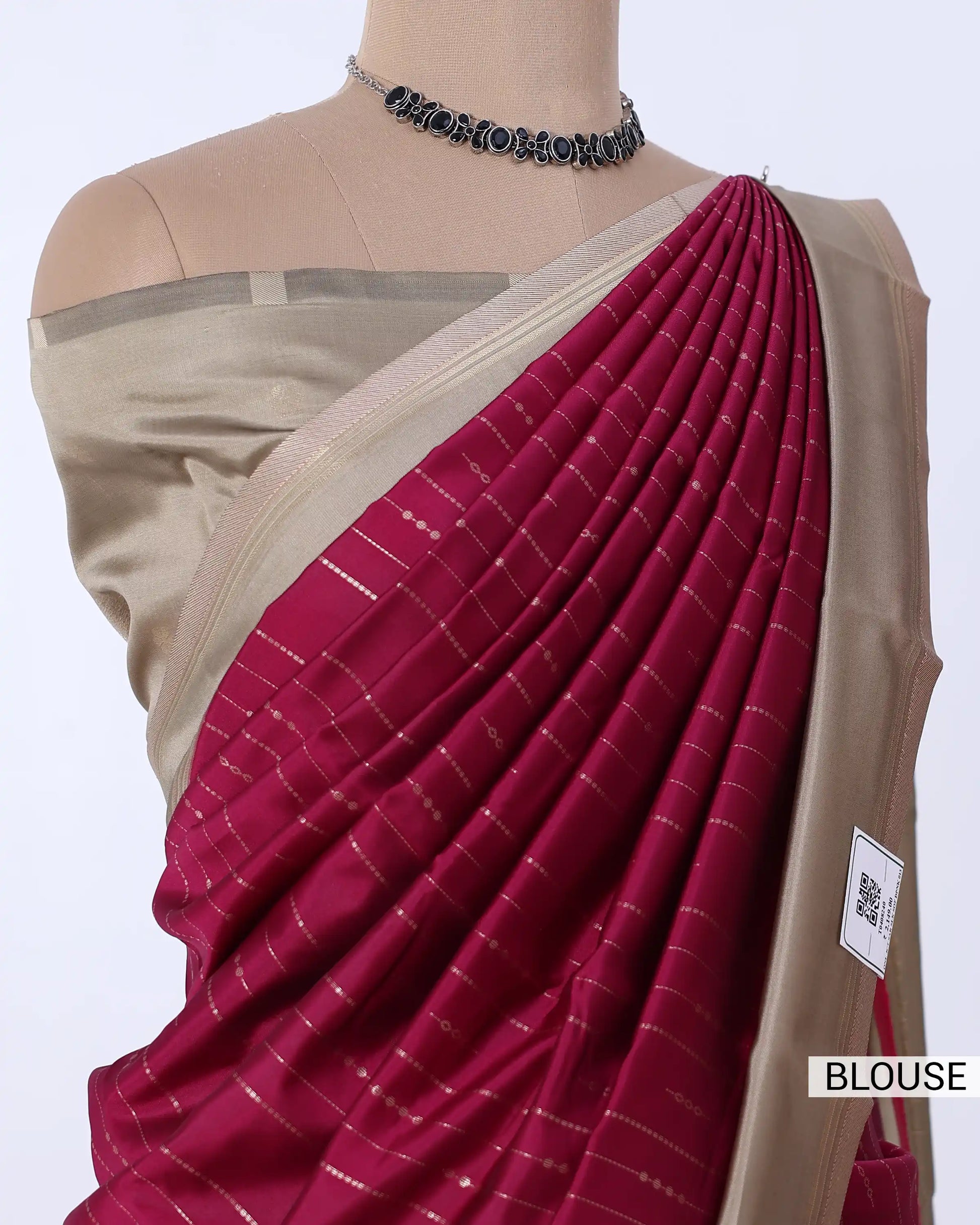 A close-up of a draped saree , featuring a deep magenta-pink body with fine silver stripes and a beige blouse. 