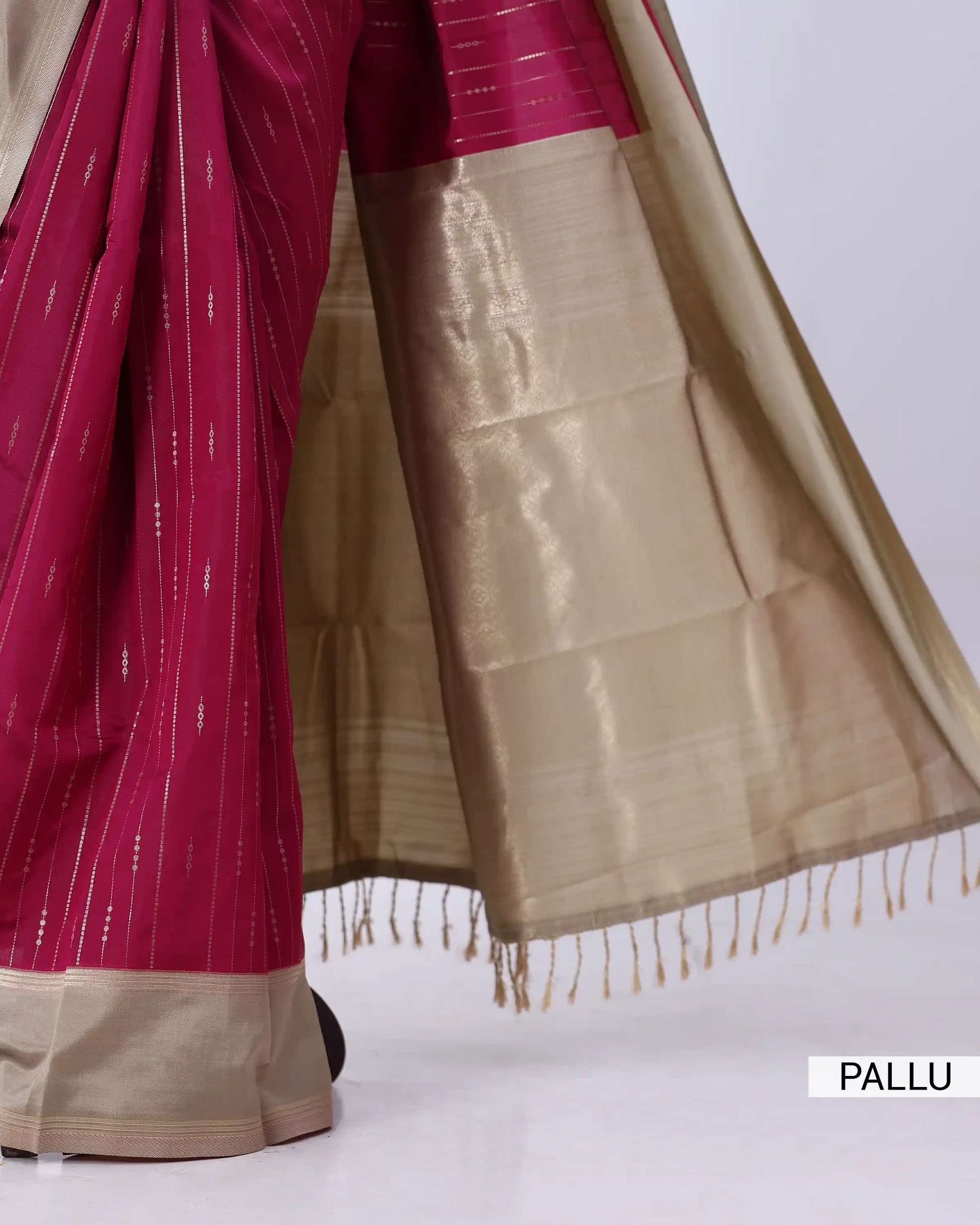 A close-up of a traditional Indian saree, showing the rich magenta-pink body with fine vertical metallic stripes 
