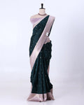 A dark green silk saree with small white motifs and a light pink border