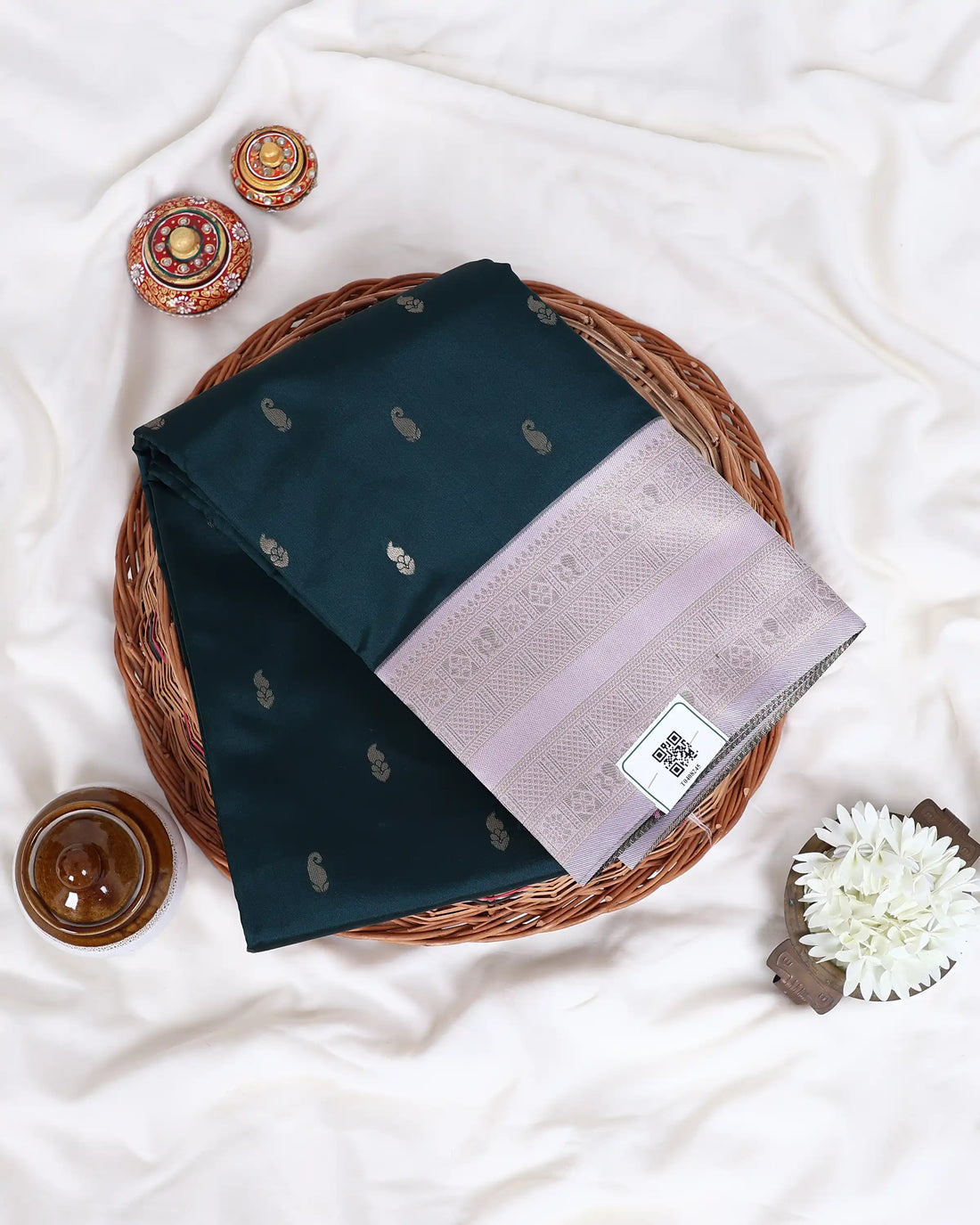 A dark green silk saree with small white motifs and a light pink border