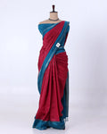 A two-tone saree  has a deep red body with a teal blue border and pallu, featuring subtle vertical stripes.