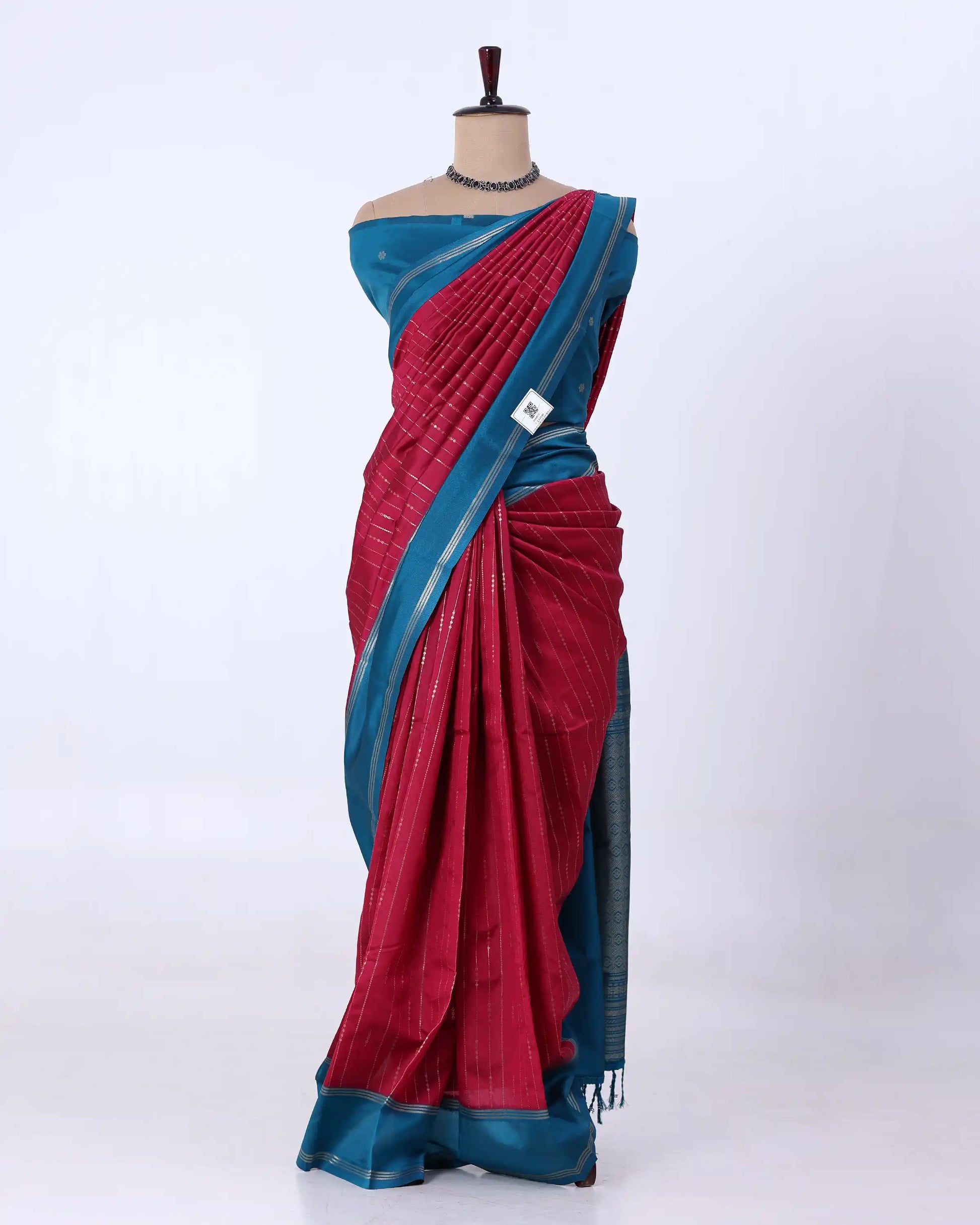 A two-tone saree  has a deep red body with a teal blue border and pallu, featuring subtle vertical stripes.