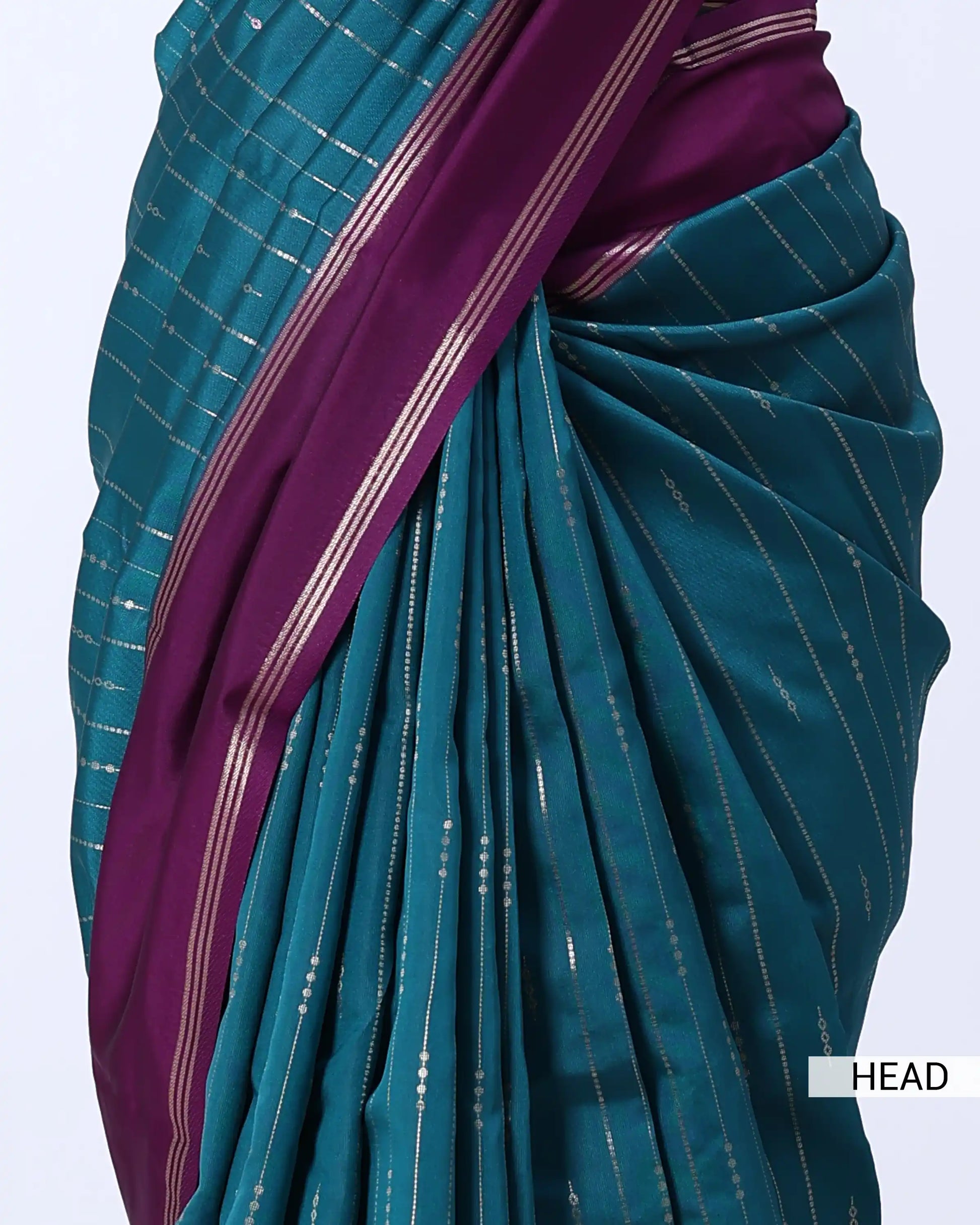 A close-up of a teal and purple sari with thin metallic gold stripes, draped to show the pleated fabric and border