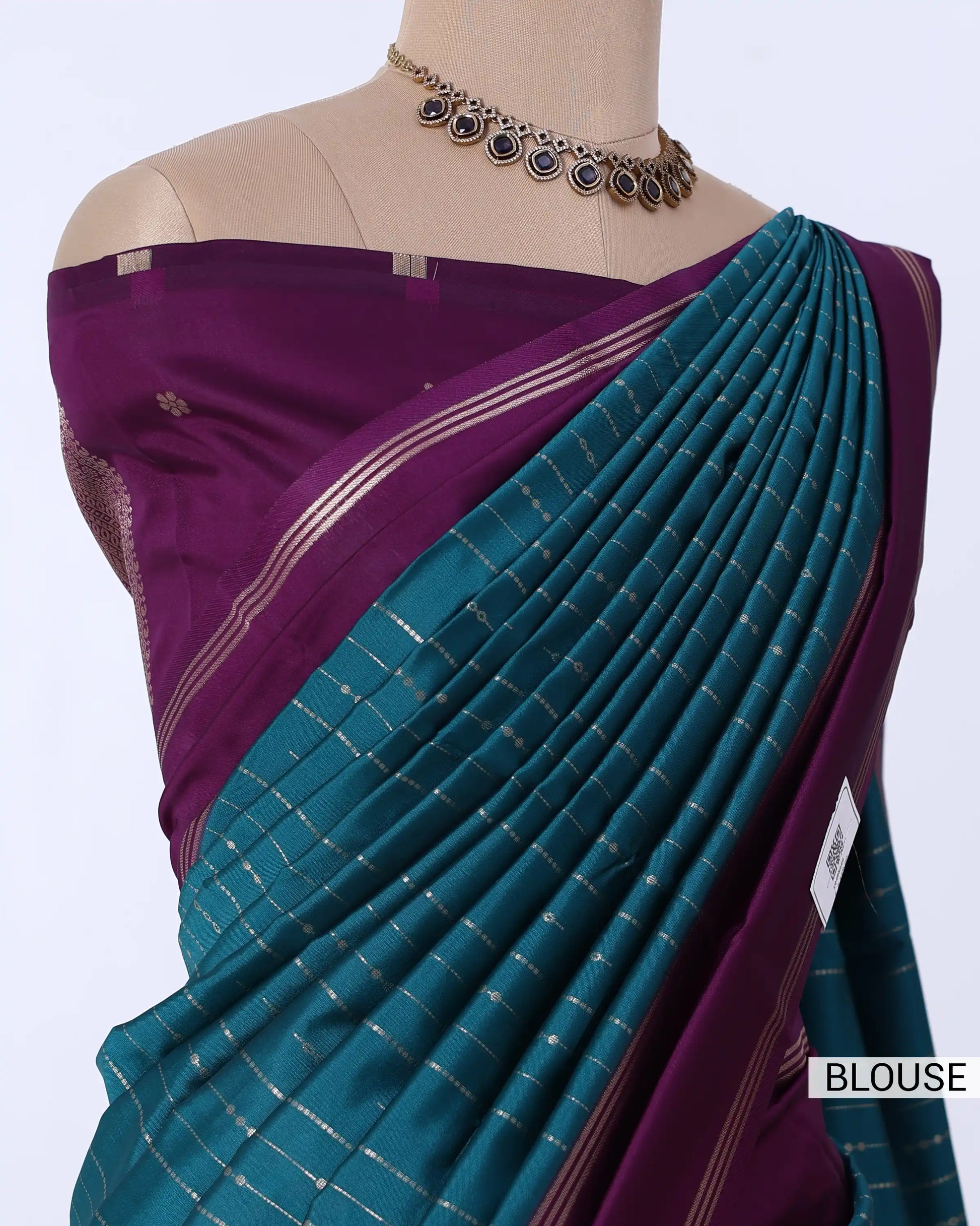 A close-up of a traditional Indian saree  featuring a deep purple blouse and a teal-green pleated drape with thin metallic stripes.