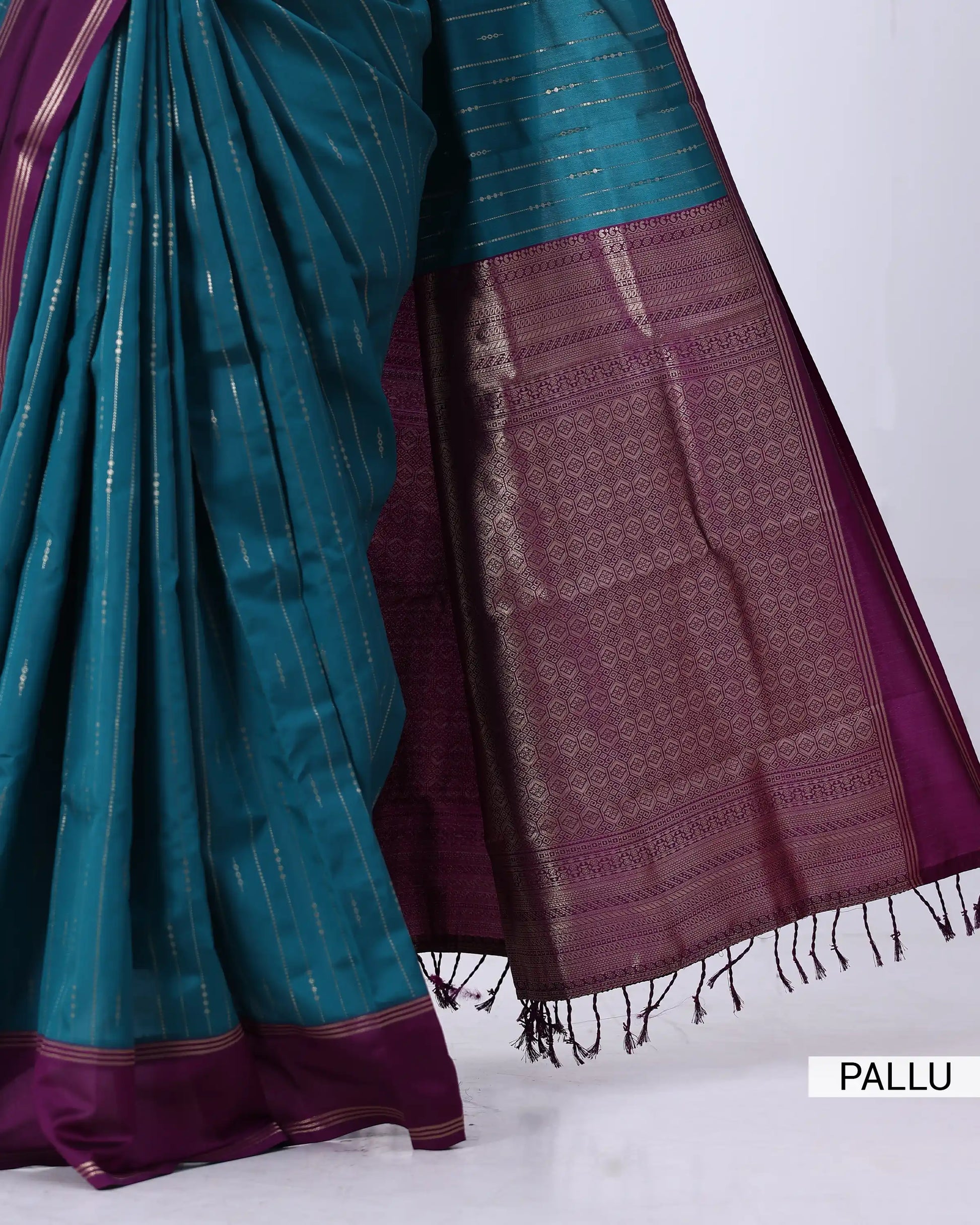 A close-up of a teal and deep purple saree with metallic gold zari detailing