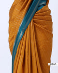 A close-up of a draped sari in mustard yellow with fine white stripes and a contrasting teal-blue border with silver stripes. 
